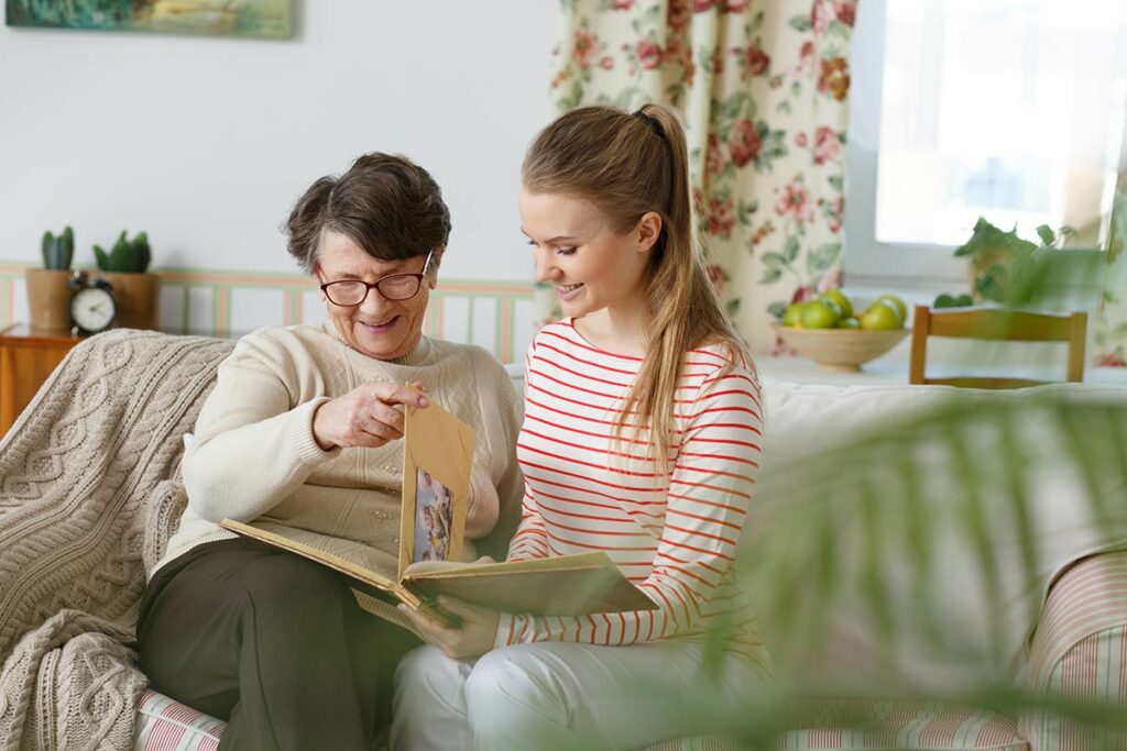 Hillcrest | Senior woman with caregiver looking at photos in living room on couch