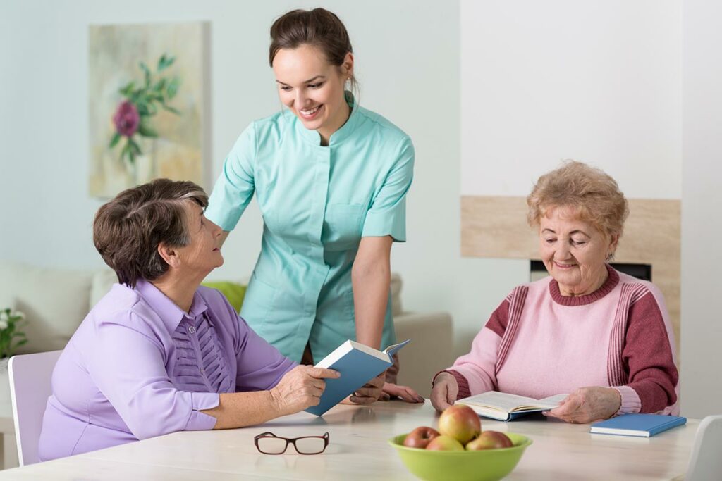 Hillcrest | Seniors reading at table with nurse caregiver
