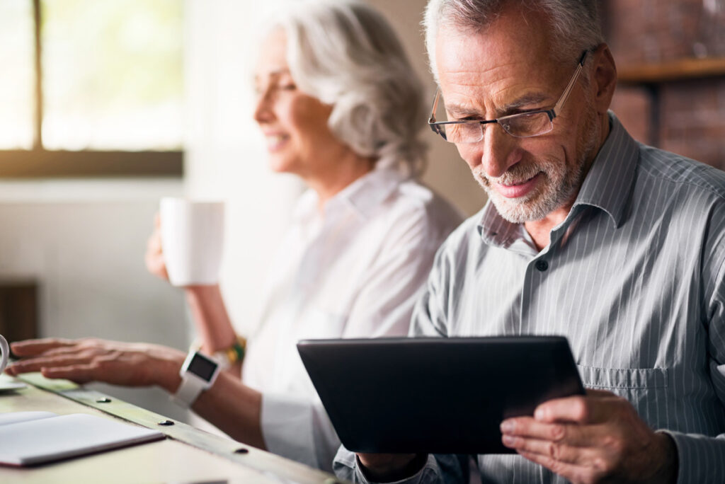 Hillcrest | Senior couple looking at their tablets and drinking coffee while smiling